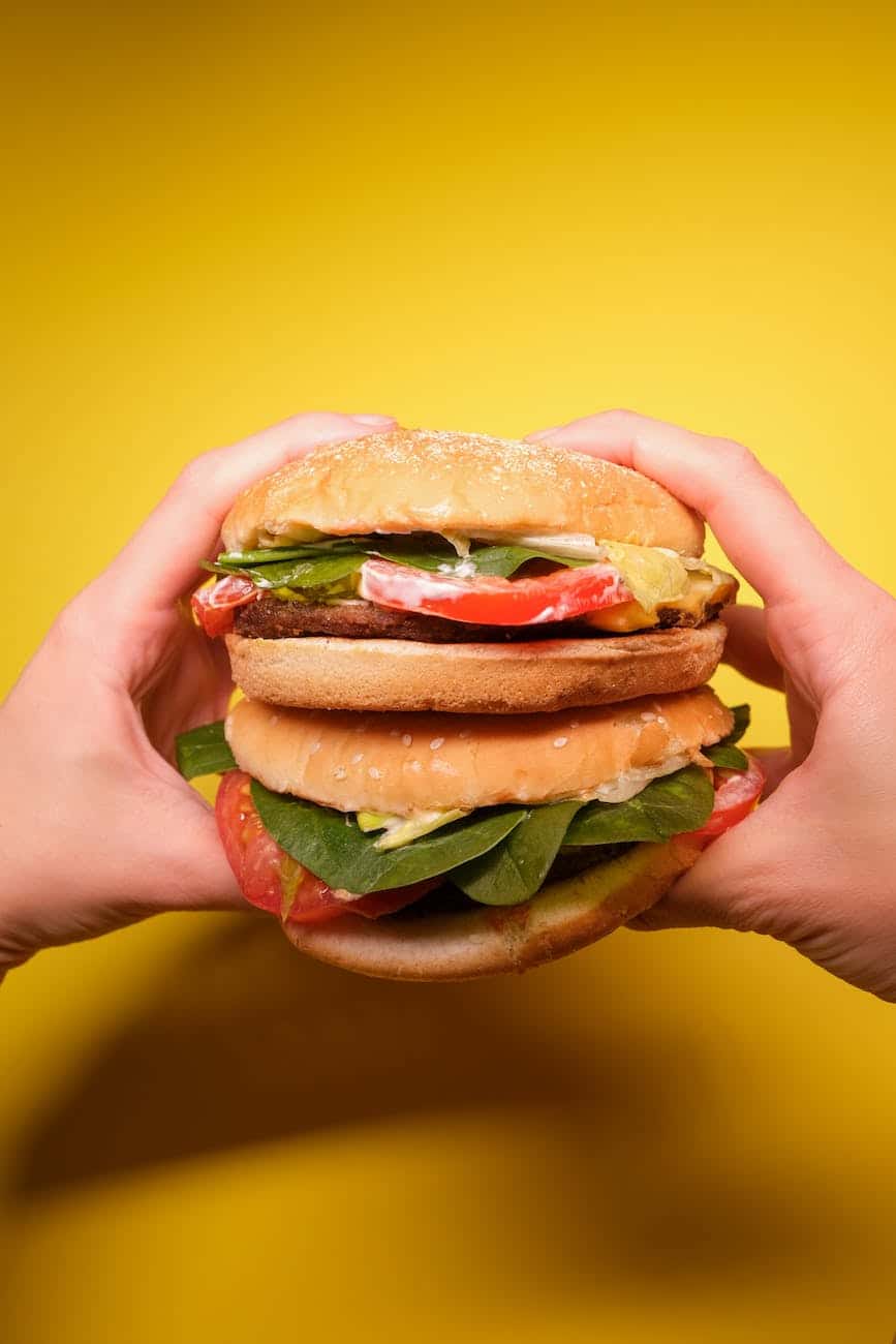 unrecognizable person with hamburgers with tomatoes near yellow wall